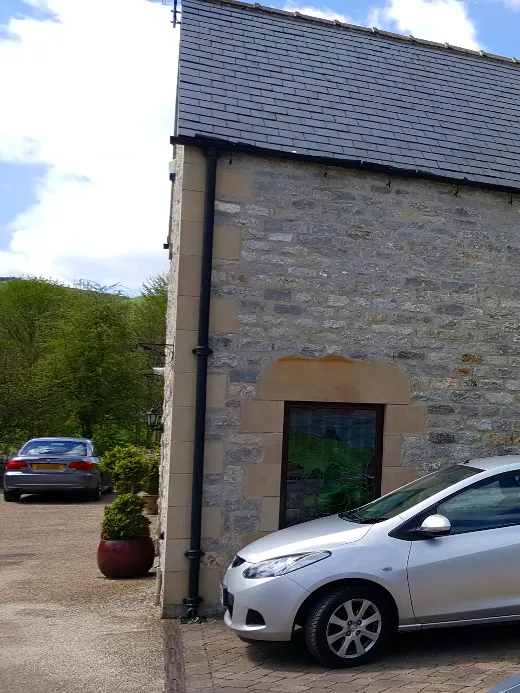 The side of a pointed stone building with a car in front.