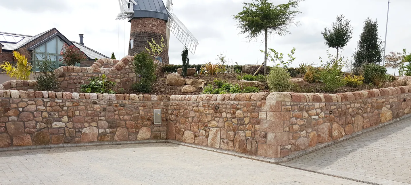 A retaining stone wall with a rockery behind and a windmill in the background.