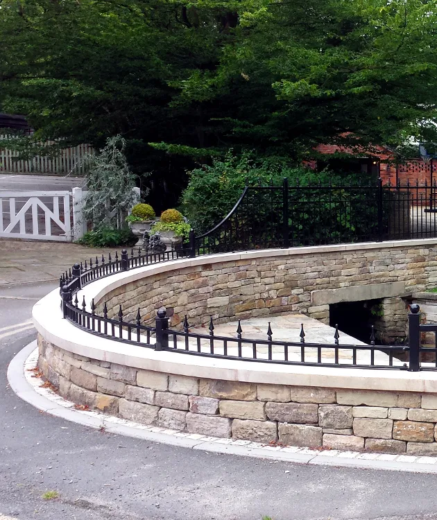 A curved stone wall with flat coping stones and wrought iron railings on top.